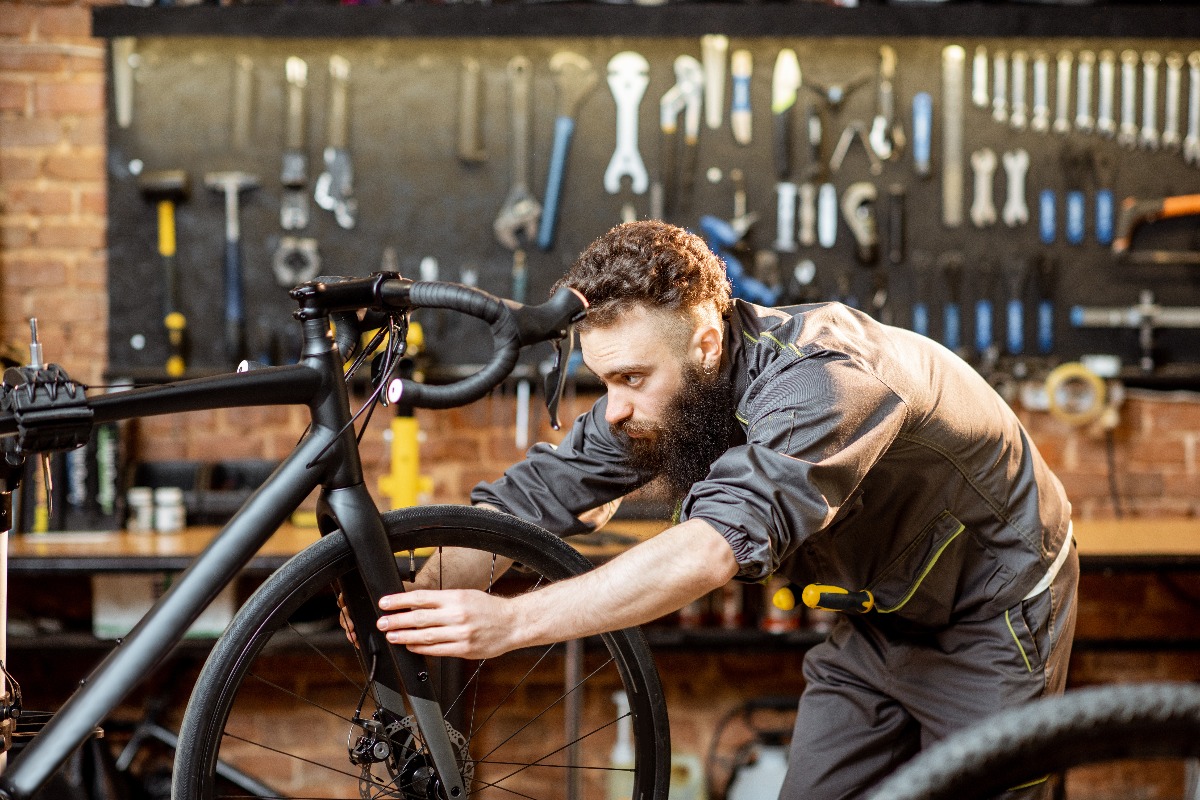Handsome bearded repairman in workwear serving a sports bike at the bicycle workshop jpg